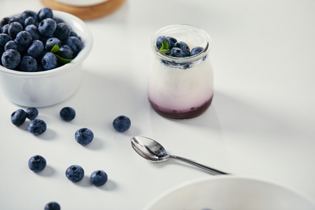 close up view of fresh blueberries and yogurt for breakfast on white tabletop with spoonの写真素材