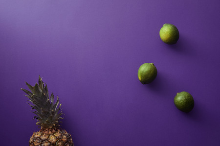 top view of pineapple and limes on violet surfaceの写真素材