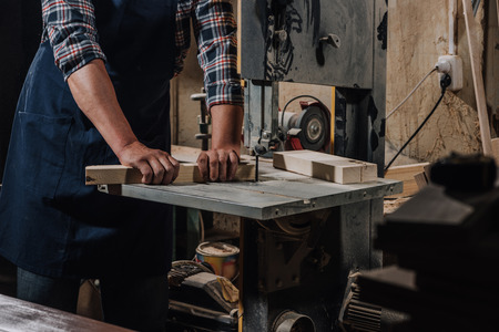 partial view of woodworker using electric drill on wood at workshop