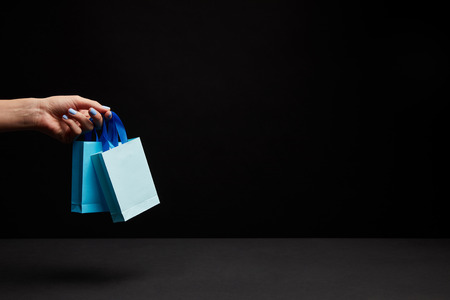 partial view of woman holding blue paper shopping bags on black backgroundの写真素材