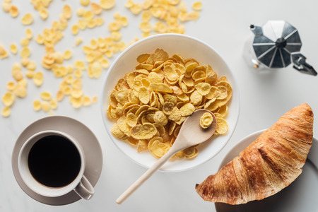 top view of bowl of corn flakes breakfast with cup of coffee and croissant on whiteの写真素材