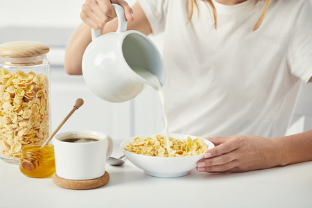 partial view of woman pouring milk into bowl with corn flakes during breakfast at homeの写真素材