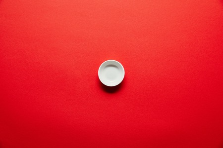 top view of white empty bowl for soya sauce on red backdropの写真素材