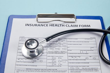 close-up view of insurance health claim form on clipboard and stethoscope on blueの写真素材