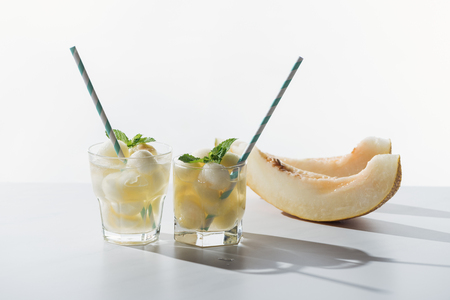 slices of sweet honeydew melon and refreshing beverage with melon and mint in glasses on whiteの写真素材