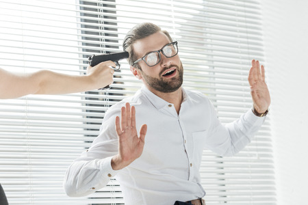 businessman raising arms while someone holding gun near his head