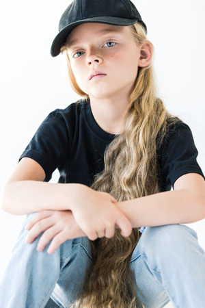 portrait of beautiful child with long curly hair wearing black cap and looking at camera isolated on whiteの写真素材