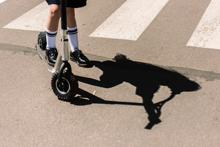 low section of little schoolgirl riding scooter on streetの写真素材