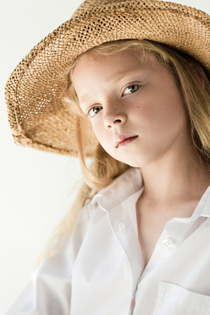 portrait of beautiful little kid in wicker hat looking at camera on whiteの写真素材