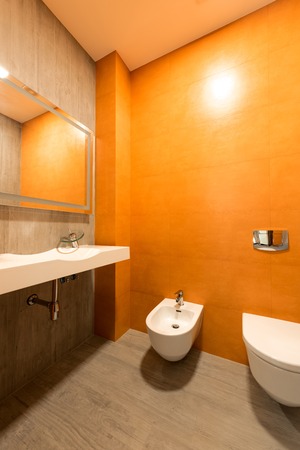 interior of modern bathroom in orange and white colors with toilet and bidetの写真素材