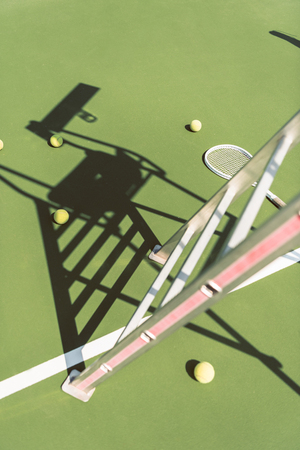 close up view of metal referee chair , tennis racket and balls on green tennis courtの写真素材