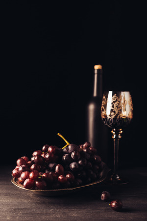fresh ripe grapes, glass and bottle of wine on wooden table on blackの写真素材