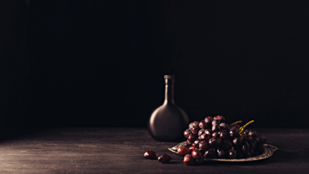 fresh ripe grapes on vintage plate and bottle of wine on wooden table on blackの写真素材