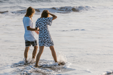 back view of couple holding hands and walking in ocean in bali, indonesiaの写真素材