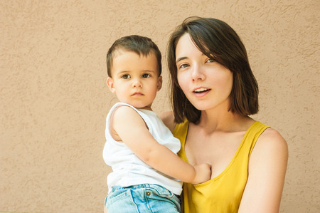 mother and son looking at camera on street near beige wallの写真素材