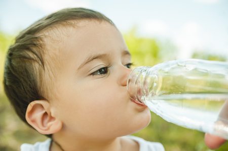 headshot of adorable toddler boy drinking water from plastic bottle in parkの写真素材