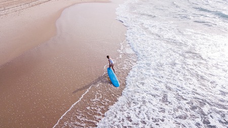 aerial view of young woman in white swimsuit pulling surfboard on sandy beach, Ashdod, Israelの写真素材