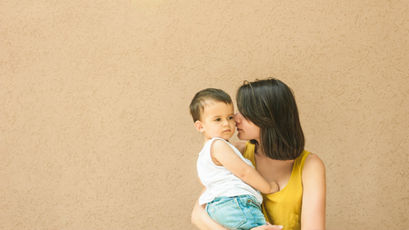 mother touching son cheek on street near beige wallの写真素材