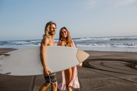 happy couple walking together on beach with surfing board in bali, indonesiaの写真素材