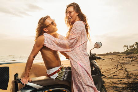 smiling couple hugging near scooter on beach during sunset in bali, indonesiaの写真素材