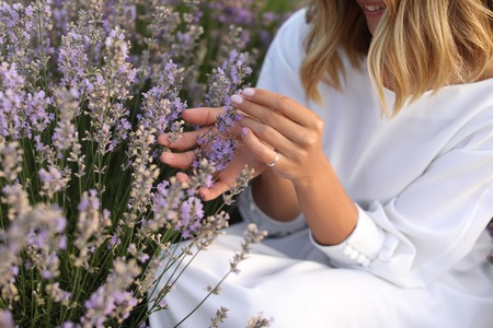 cropped image of smiling woman in white dress touching flowers in violet lavender fieldの写真素材