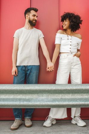 happy stylish young multiethnic couple holding hands and smiling each other on streetの写真素材