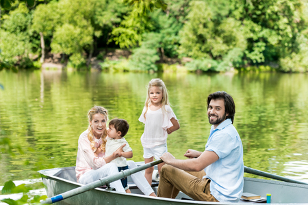 happy young family riding boat on lake at park and looking at cameraの写真素材