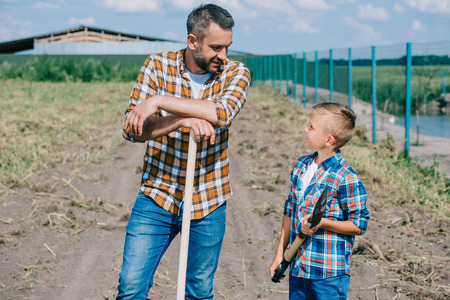 father and son holding shovels and looking at each other on farmの写真素材