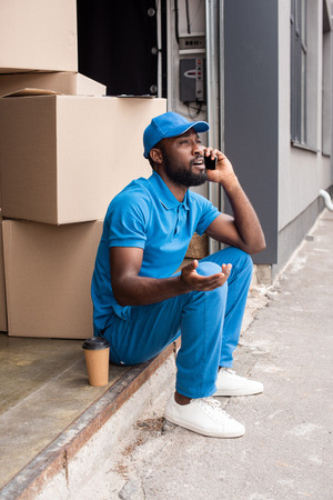 african american delivery man gesturing and talking by smartphoneの写真素材