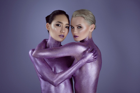 multiethnic nude girls in ultra violet glitter embracing for fashion shoot, isolated on purpleの写真素材