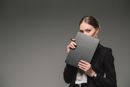 businesswoman covering face by textbook isolated on grey backgroundの写真素材
