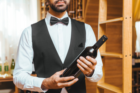 cropped shot of young wine steward with bottle of luxury wine at wine storeの写真素材