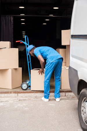 side view of african american delivery man putting boxes on cartの写真素材