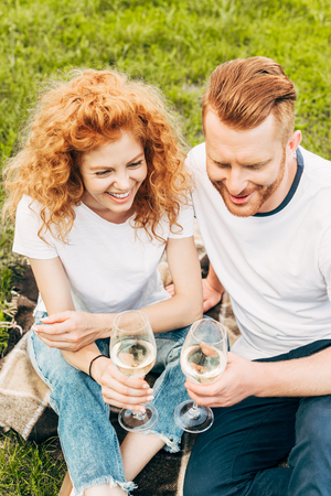 high angle view of happy redhead couple holding glasses of wine at picnic in parkの写真素材