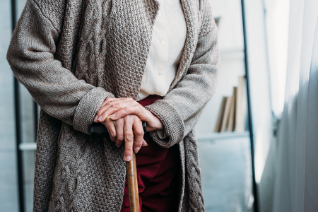 cropped shot of senior lady with wooden walking stick standing at homeの写真素材