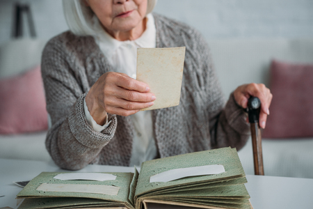 partial view of senior woman looking at photo from photo album at table at homeの写真素材