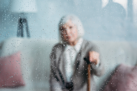 selective focus of grey hair lady with walking stick resting on sofa at homeの写真素材