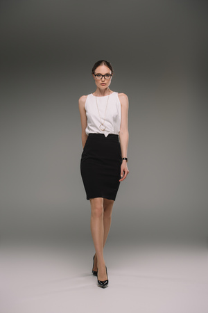 beautiful businesswoman in eyeglasses walking on grey backgroundの写真素材