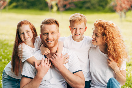 beautiful happy redhead family hugging and smiling at camera in parkの写真素材