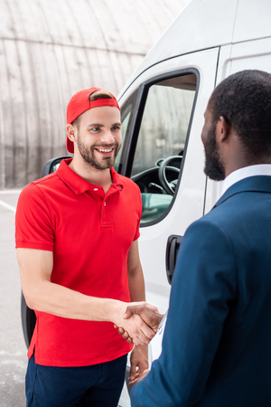 smiling delivery man and african american businessman shaking handsの写真素材