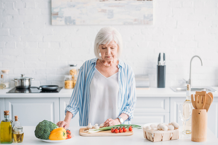 portrait of senior lady cutting vegetables while cooking dinner at counter in kitchenの写真素材