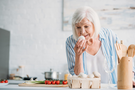 portrait of grey hair lady checking mushrooms while cooking dinner at counter in kitchenの写真素材