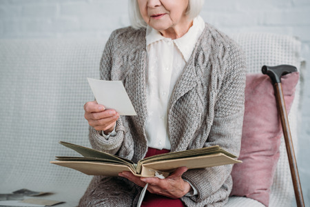 cropped shot of senior lady with photo album sitting on couch at homeの写真素材