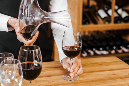 cropped shot of sommelier pouring wine from decanter at wine store