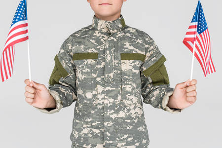 cropped shot of child in military uniform with american flagpoles in hands isolated on greyの写真素材