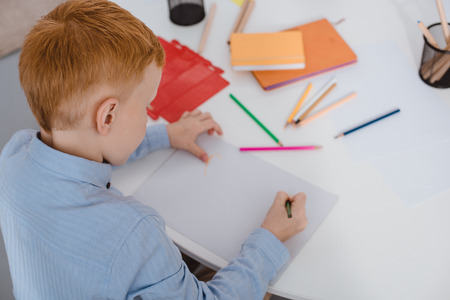 high angle view of red hair boy drawing picture with pencils at table