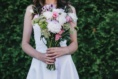 cropped view of bride in traditional white dress holding wedding bouquetの写真素材