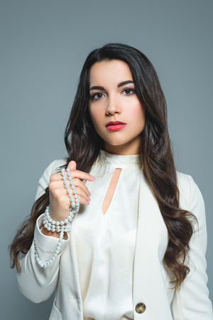 portrait of attractive girl posing in white suit with necklace, isolated on greyの写真素材