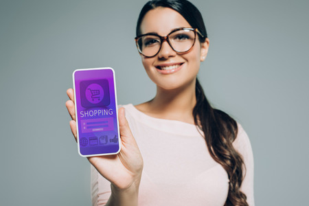 beautiful woman presenting smartphone with online shopping appliance, isolated on greyの写真素材