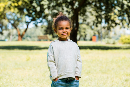 adorable african american kid in jeans and sweater looking at camera in parkの写真素材